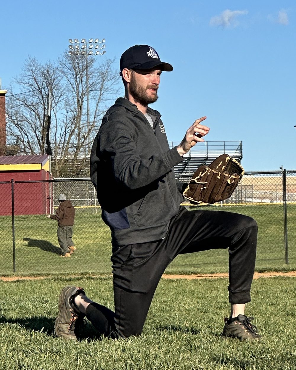 Coach Mark kneeling on the field with a glove, demonstrating a throw