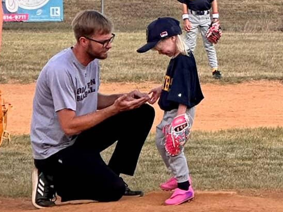 Coach Mark kneeling on the mound, showing a young player a grip